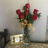 Red roses in a clear vase with a gold ribbon and chocolate box beside it