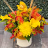 Yellow and orange floral arrangement in a white vase with autumn leaves