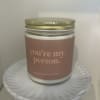 Glass jar candle with gold lid and label reading "you’re my person" on a white pedestal stand.