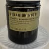 Black jar candle with a tan label on a white pedestal
