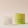 Lit white candle in a clear glass vessel beside a lime-green candle tin