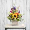 Colorful mixed flower arrangement in a wooden box with a candle beside it