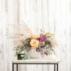 Peach roses and purple flowers in a white vase with airy dried grass