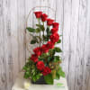Tall arrangement of red roses in a black container with a candle nearby