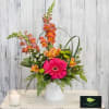 Bright mixed flower arrangement in a white vase with a candle nearby