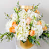 White and peach floral arrangement in a gold hatbox-style container