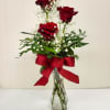 Three red roses in a clear glass vase with a red ribbon