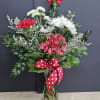 Bouquet of red carnations, white daisies, and pink alstroemeria in a glass vase with a red polka-dot ribbon.