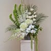 Tall white floral arrangement with orchids, roses, and palm fronds in a gray vase