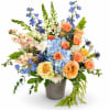 Mixed bouquet of blue, peach, and white flowers in a textured vase