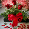 Red roses in a glass vase with a red ribbon and heart confetti