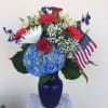 Red, white, and blue floral arrangement in a blue vase with an American flag