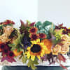 Autumn floral arrangement with sunflowers, roses, and chrysanthemums in a low container