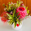 Bright tropical bouquet with a large pink protea in a white vase