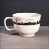 White ceramic mug with a black city skyline and labeled landmarks around the rim.