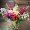 Mixed bouquet of pink, white, and blue flowers in a clear glass vase