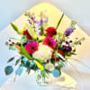 Bouquet of red roses, pink gerbera daisies, white hydrangea, and purple blooms in a glass vase