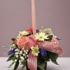 Pink candle in a mixed flower arrangement with a striped ribbon