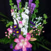 Pink lilies and purple flowers in a glass vase with a purple ribbon