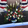 Large memorial floral arrangement with white calla lilies, roses, and blue flowers