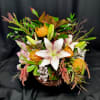 Tropical flower arrangement with white lilies and orange pincushion blooms in a basket.