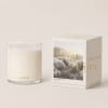 White candle in a clear glass jar beside a boxed candle set