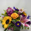 Mixed bouquet with sunflowers, pink lilies, and an orange rose in a glass vase