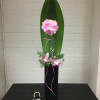 Tall floral arrangement with pink blooms, orchids, and a large green leaf in a black vase