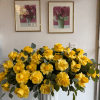 Large arrangement of yellow roses with round foliage in a white pedestal vase against a gallery wall