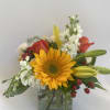 Mixed bouquet with a sunflower, lilies, roses, and white blooms in a glass vase