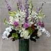 Tall bouquet of white orchids, lilies, hydrangeas, and purple roses in a glass vase