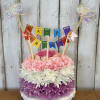 Birthday cake made of pink, white, and purple flowers with a banner topper