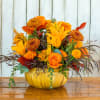 Orange and yellow floral arrangement in a pumpkin-shaped container