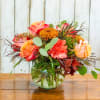 Mixed bouquet of orange, pink, and yellow flowers in a glass vase