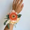 Peach and cream wrist corsage with ribbon and greenery on a hand
