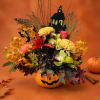 Halloween floral arrangement in a jack-o'-lantern container with a haunted house topper