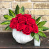 Red roses arranged in a white pumpkin-shaped vase with variegated leaves