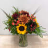 Mixed bouquet in a clear glass vase with sunflowers, chrysanthemums, and spray roses
