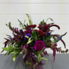Mixed bouquet of burgundy, purple, and blue flowers in a clear vase