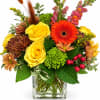 Mixed bouquet of yellow roses, orange gerbera daisies, and chrysanthemums in a glass vase