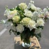 White roses and small white flowers arranged in a clear glass vase