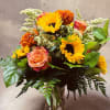 Bouquet of sunflowers, roses, and orange carnations in a glass vase