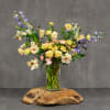 Mixed pastel flowers in a clear glass vase on a wooden base