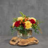 Red roses and yellow mums in a clear square vase on a wood slab