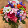 Mixed bouquet of pink, purple, orange, and white flowers in a glass vase