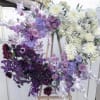 Large heart-shaped floral arrangement in purple, white, and burgundy tones on an easel