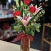 Red roses and pink lilies in a clear glass vase with a red ribbon