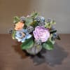 Small pastel floral arrangement in a silver vase with blue and lavender blooms