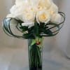 White rose bouquet in a tall glass vase with looping green leaves