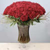 Tall bouquet of red carnations with feathery accents in a clear pedestal glass vase